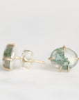 A pair of gold stud earrings featuring oval clear resin cabochons filled with green moss, shown on a clean white background.