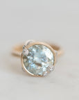 A round bezel-set ring featuring a light blue aquamarine gemstone in a gold-toned setting, photographed on a light gray background.