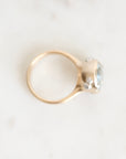 A gold ring with a large oval light blue gemstone and small clear accent stones, photographed on a light marble-like surface.