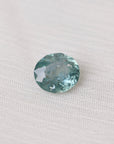 Greenish-blue gemstone on a white fabric background