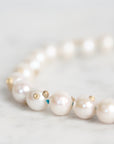 A close-up of a pearl strand necklace with small gold and blue bead accents, resting on a light marble surface.