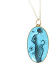 A turquoise pendant with a scrimshaw mermaid illustration on a long silver chain.