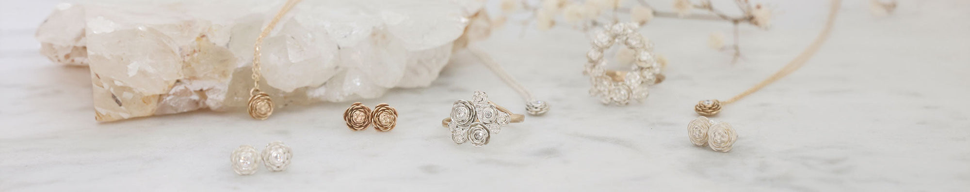 four rings and two pairs of studs laying on marble in a group. All have rose blossom details.
