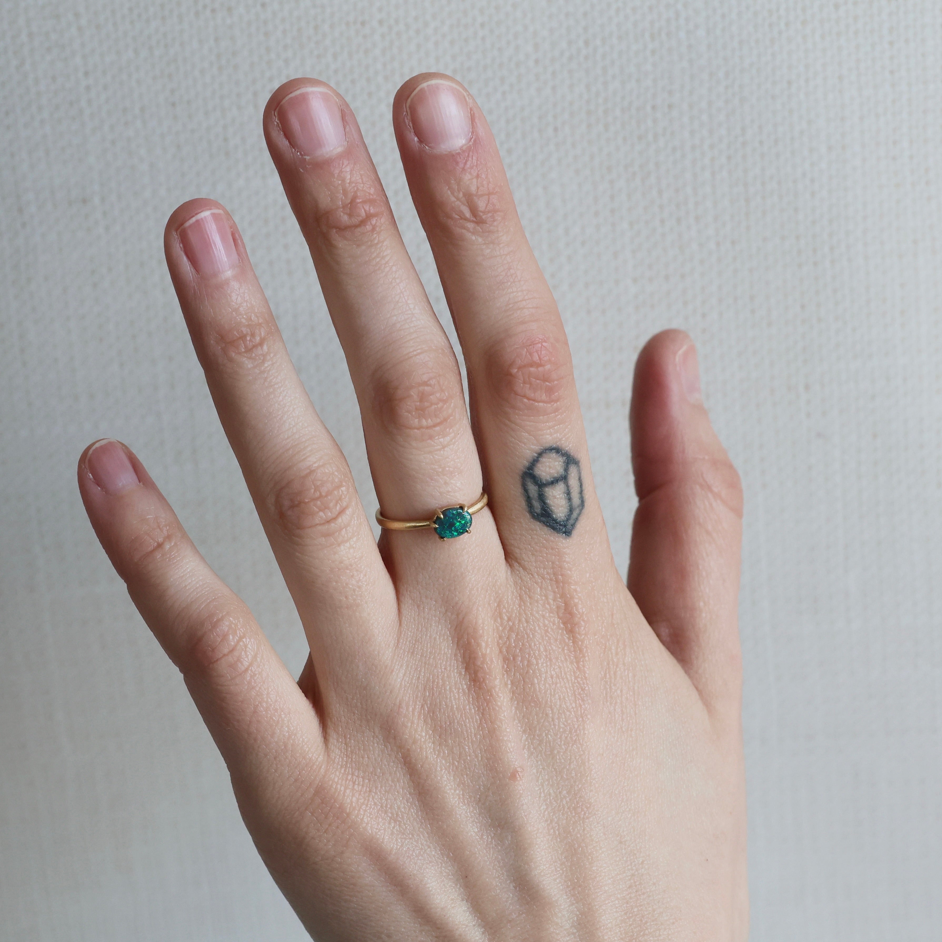 Hand wearing a gold ring with a green gemstone on a neutral background