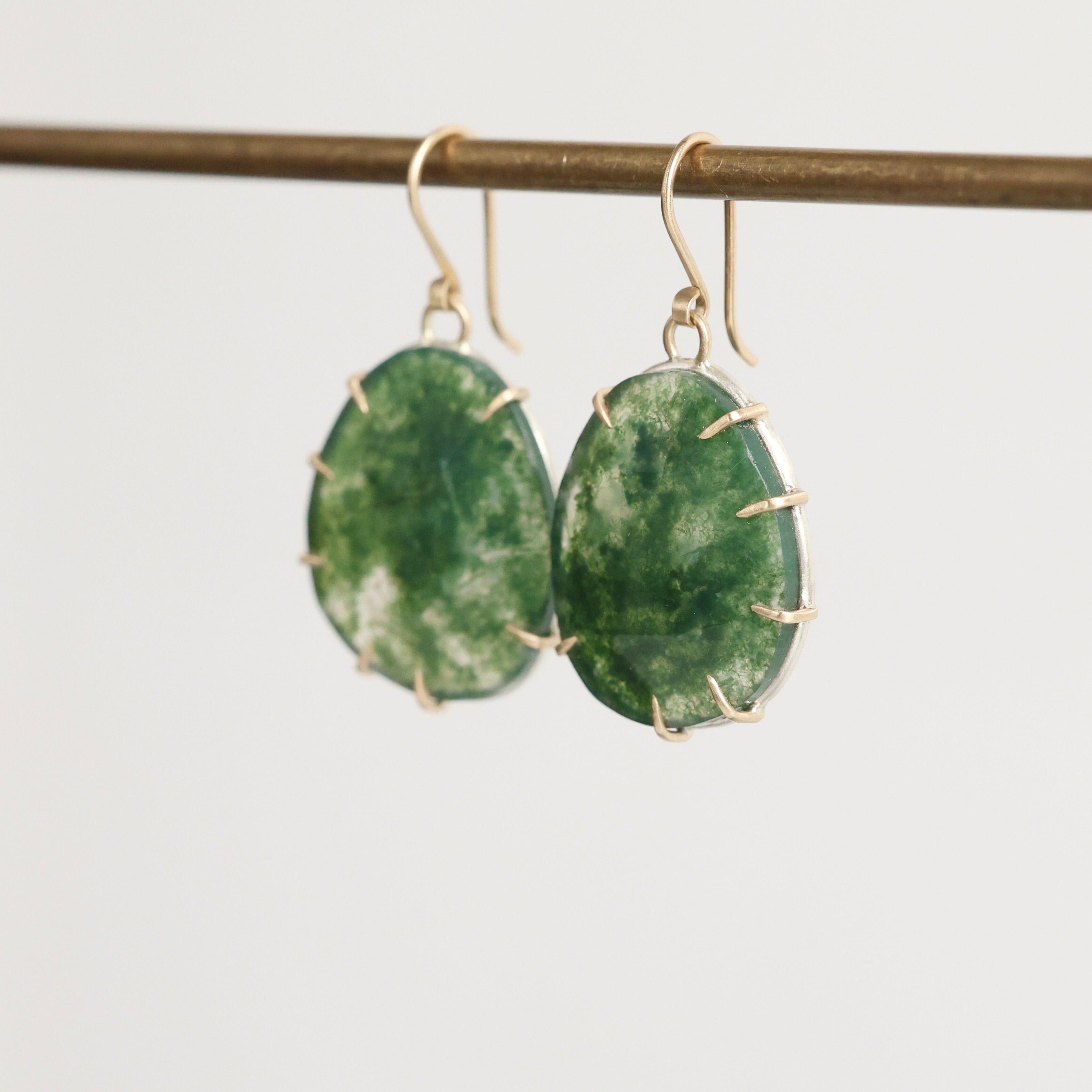 Green stone earrings on a thin rod against a light background
