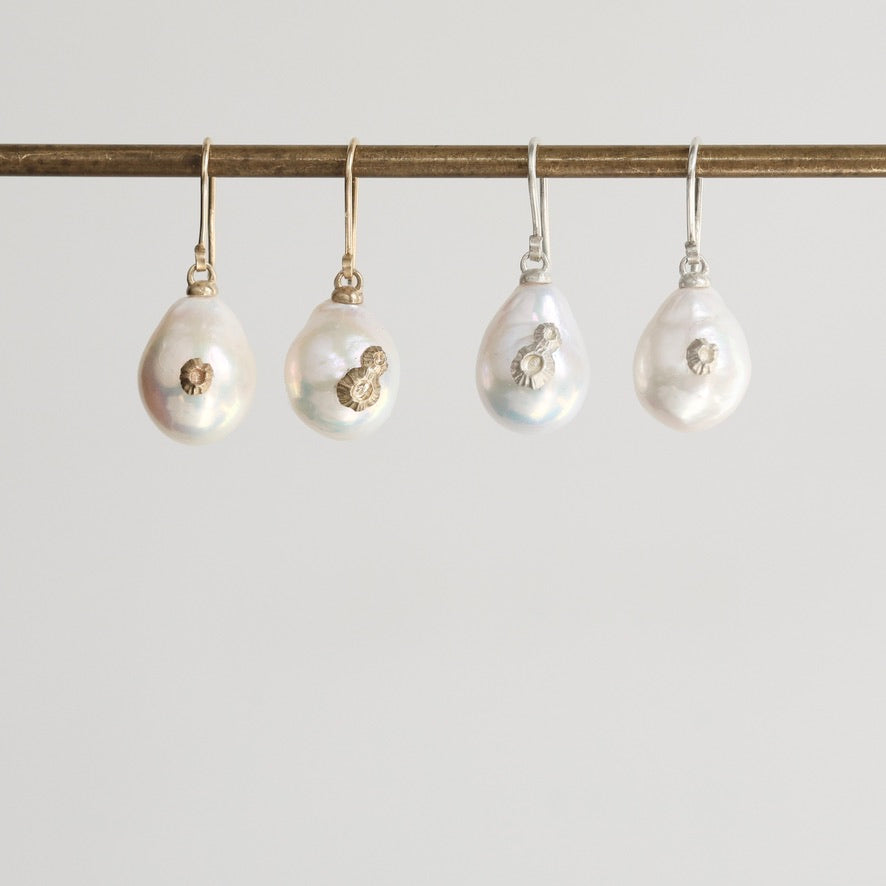 Four pearl earrings hanging on a rod against a light gray background