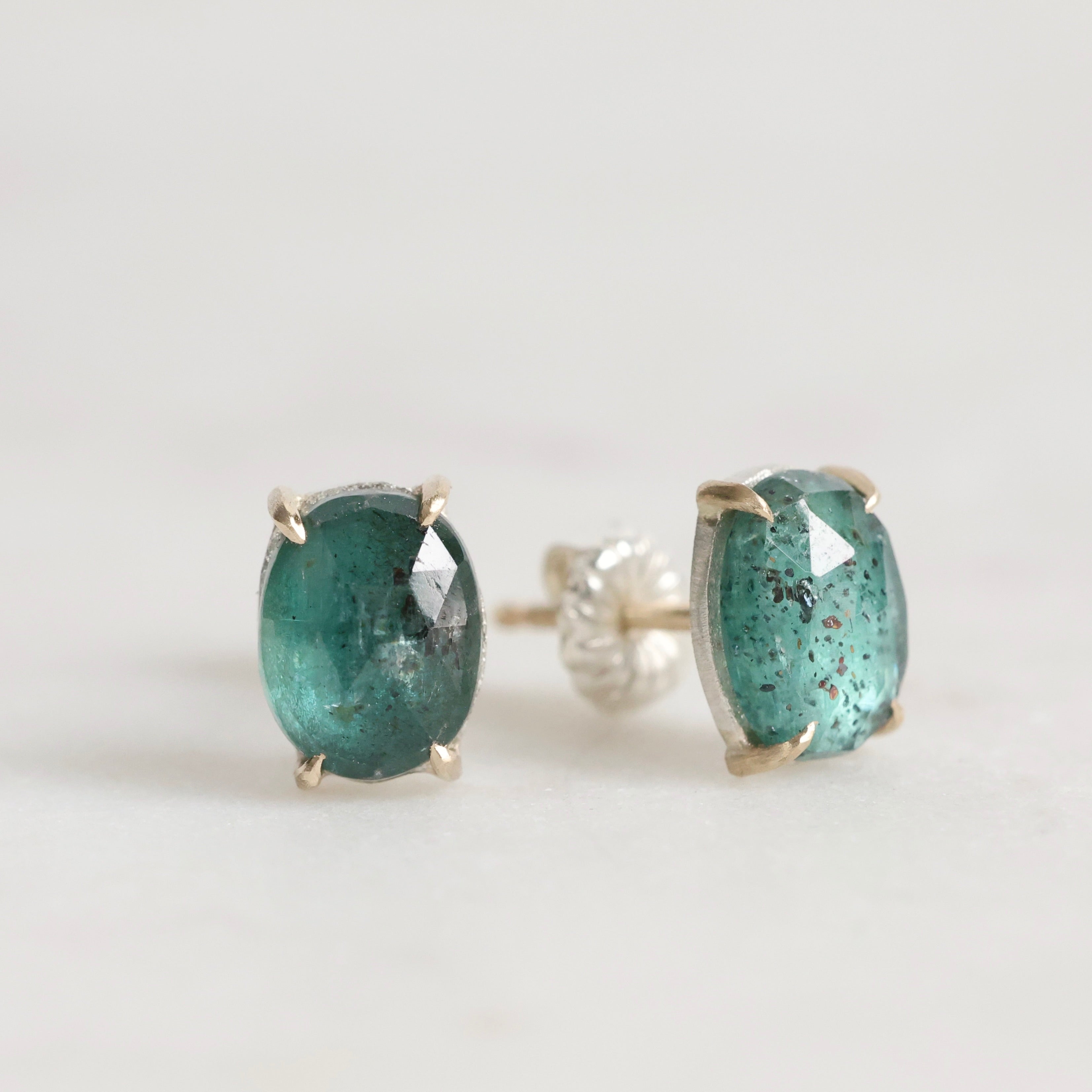 Pair of green gemstone stud earrings on a light gray background
