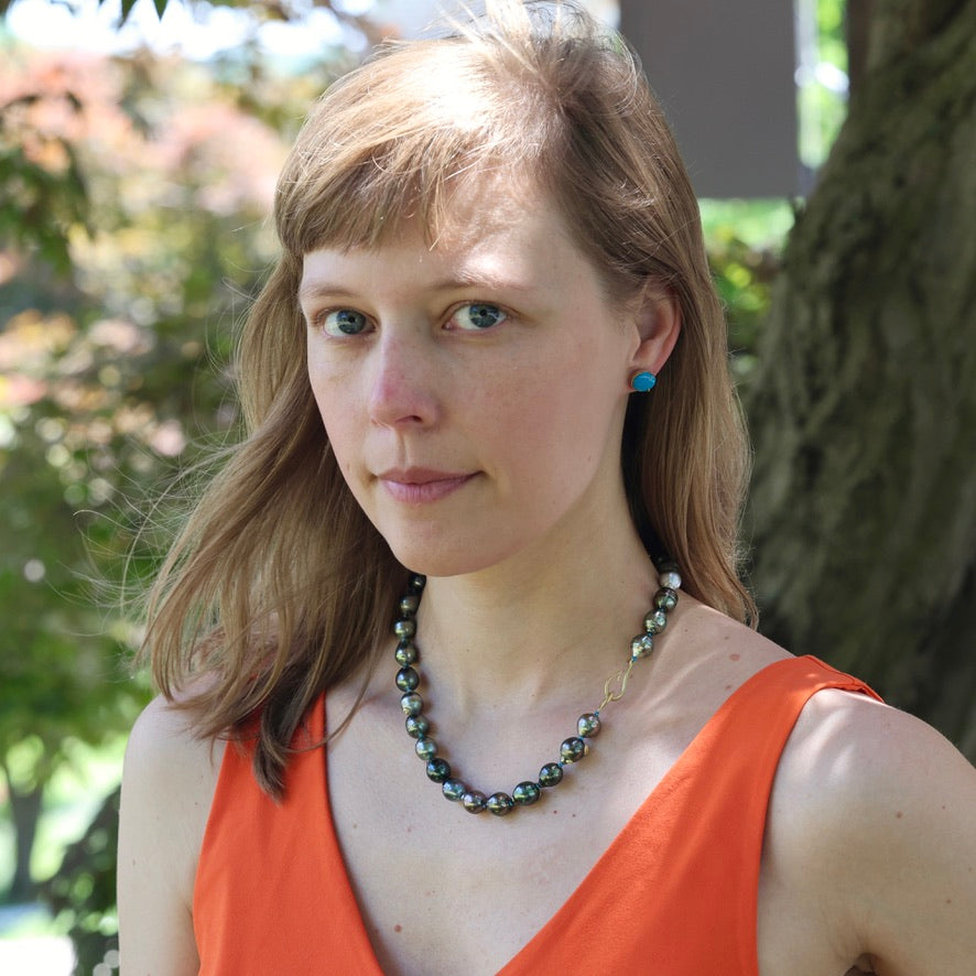 Woman wearing an orange top and a necklace with a blurred natural background