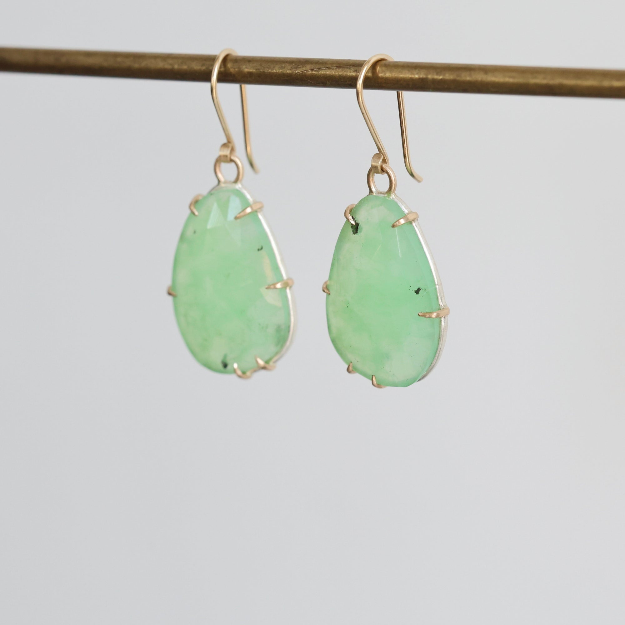 Pair of green teardrop earrings on a thin rod against a light gray background