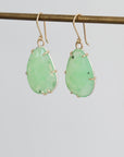 Pair of green teardrop earrings on a thin rod against a light gray background