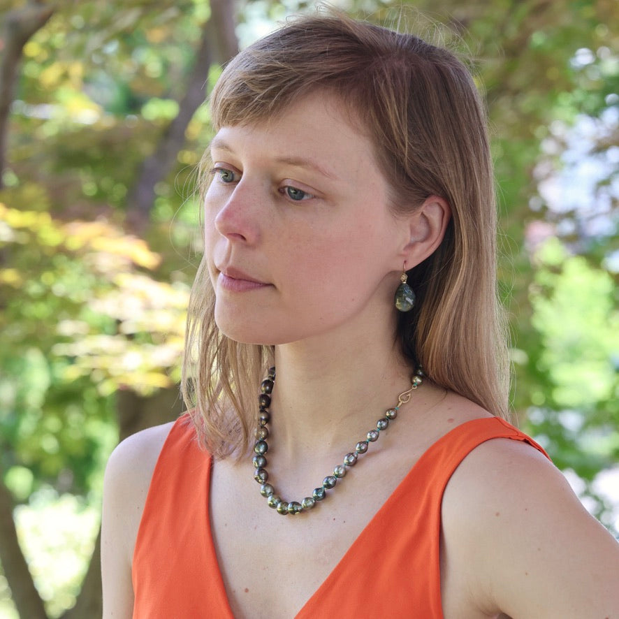 Woman wearing an orange top and a necklace with green beads outdoors