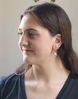 Woman with a side profile, wearing earrings, against a neutral background