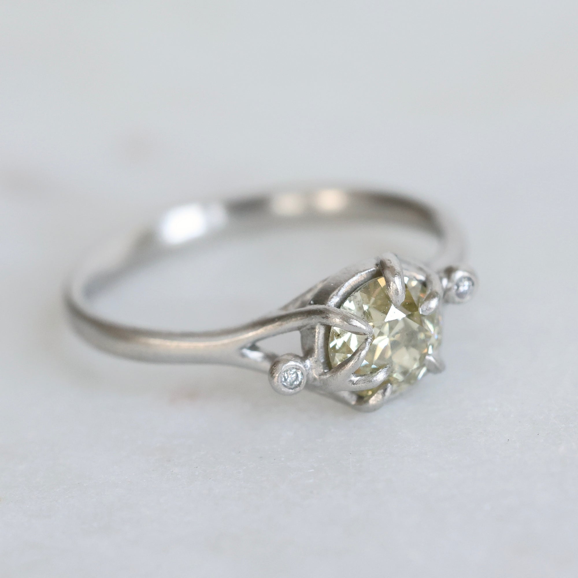 Silver ring with a large diamond and smaller stones on a light gray background