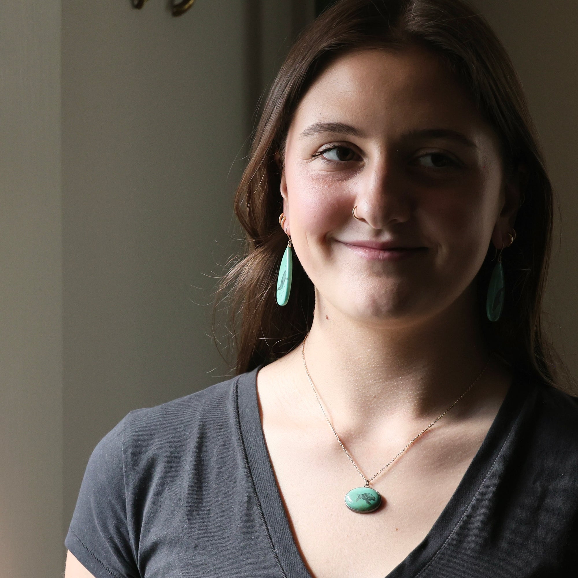 Woman wearing a necklace with a green pendant against a neutral background