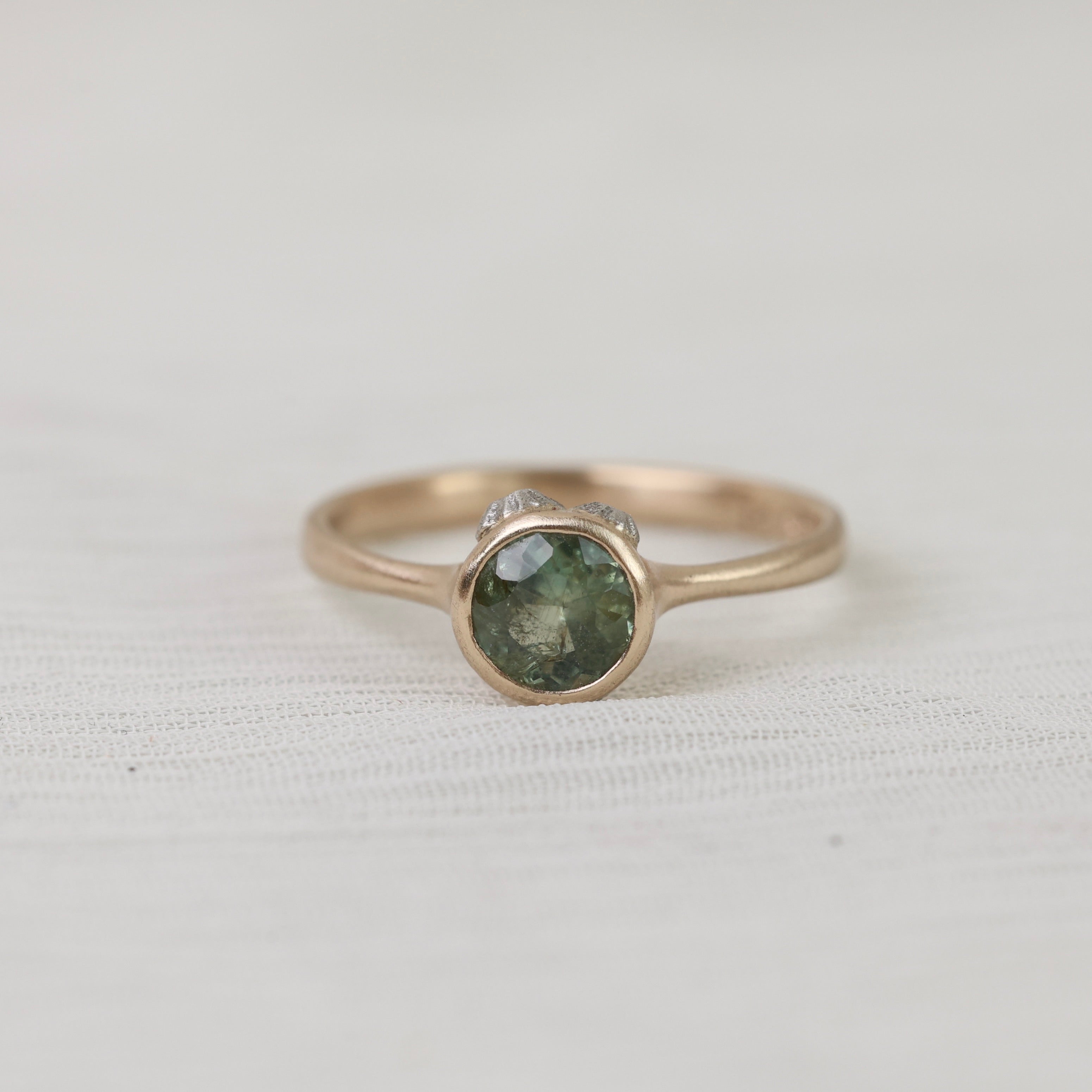 Gold ring with a green gemstone on a light gray background