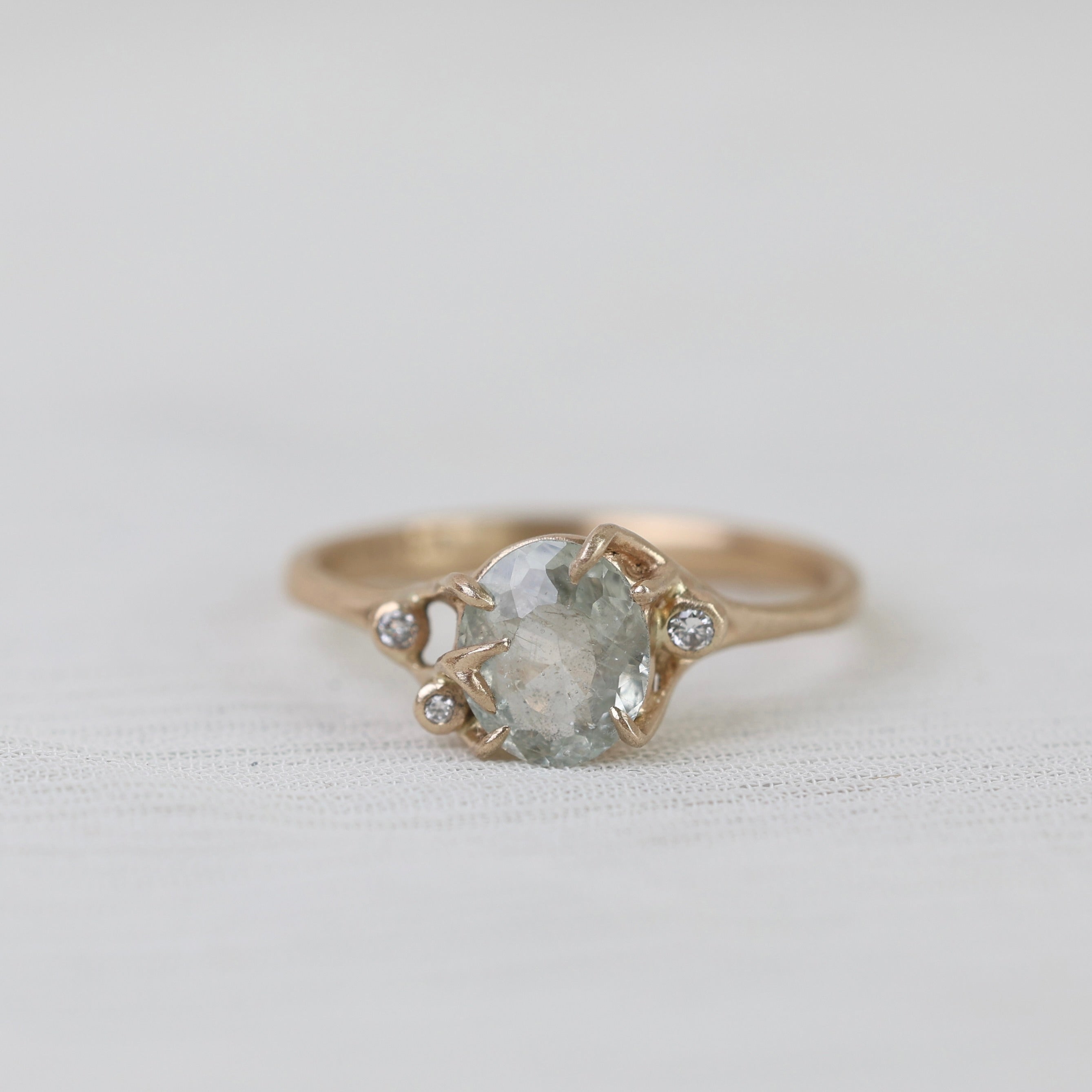 Gold ring with a large central gemstone and smaller stones on a light fabric background