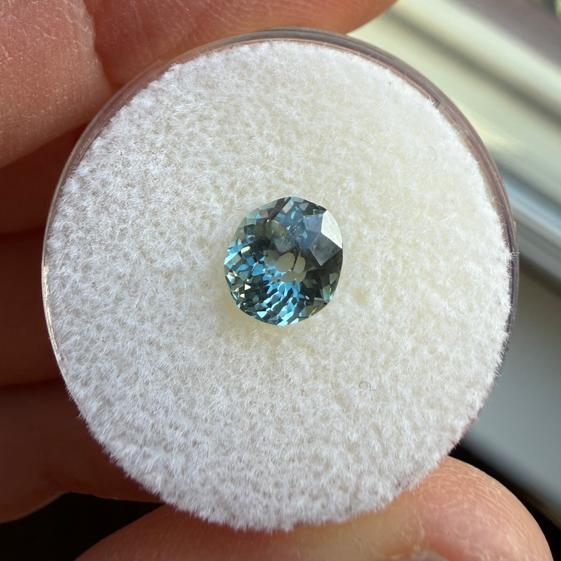 Blue gemstone on a white cushion held between fingers