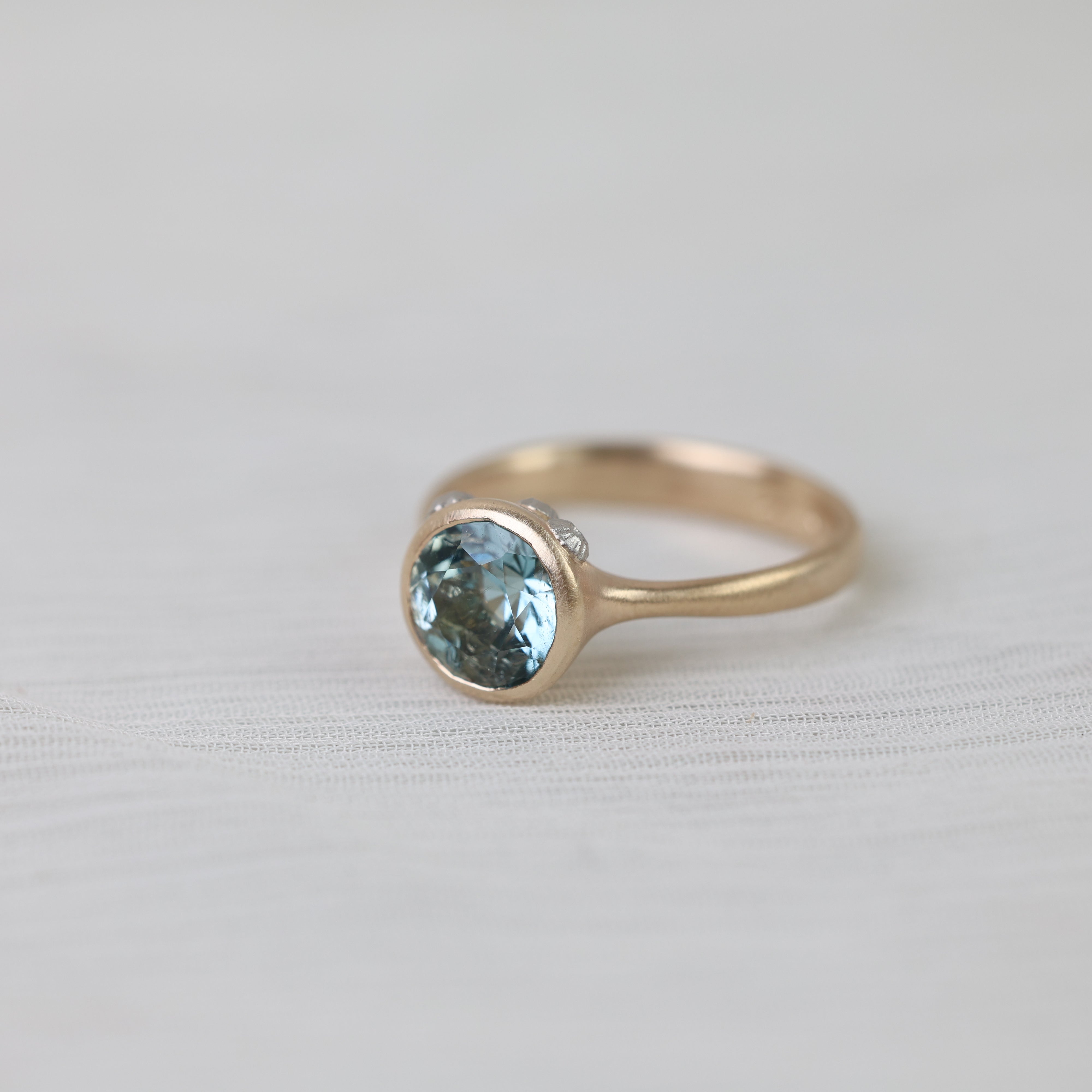 Gold ring with a blue gemstone on a light gray background