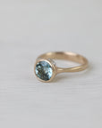 Gold ring with a blue gemstone on a light gray background