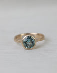 Gold ring with a blue gemstone on a light gray background