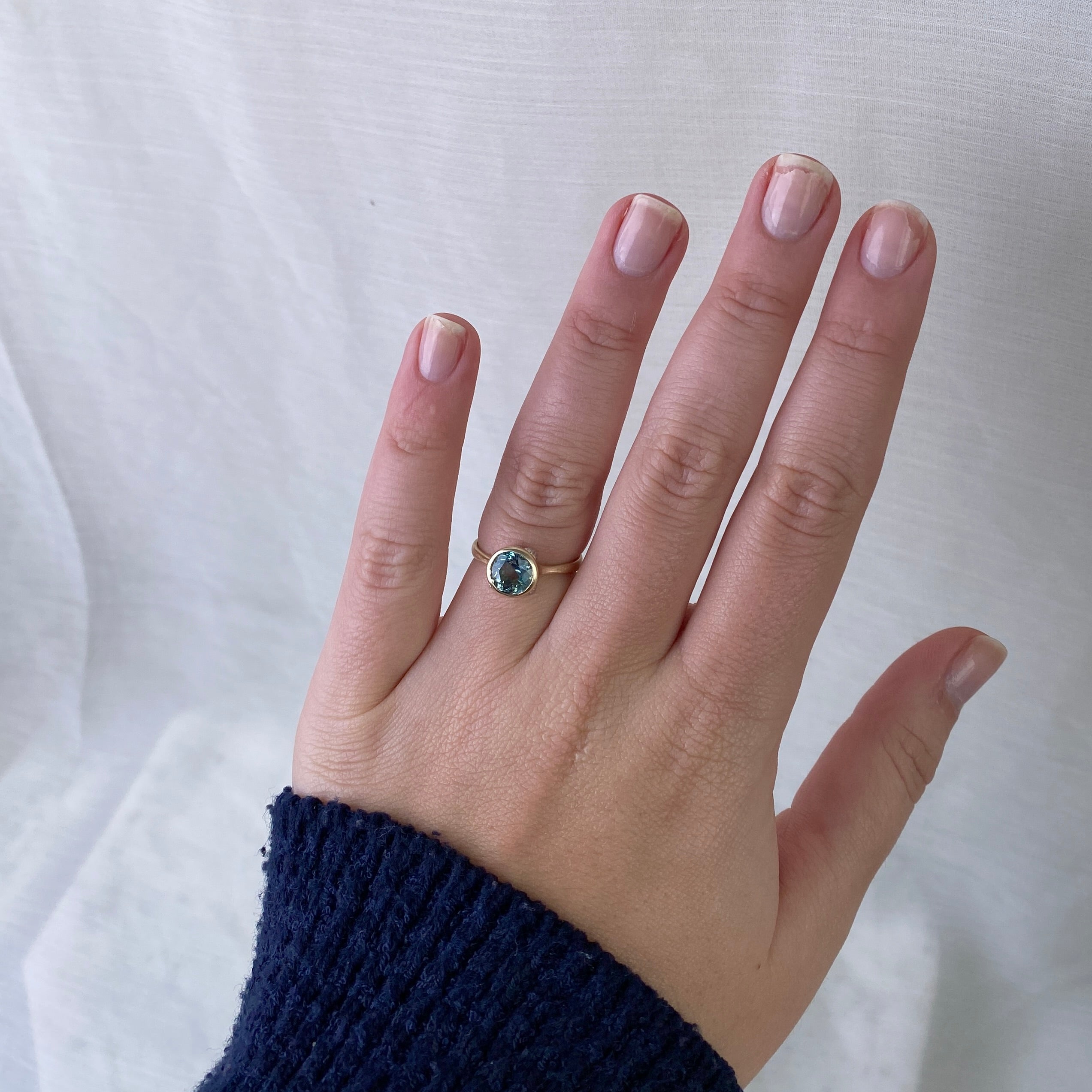 Hand wearing a gold ring with a blue gemstone on a white background