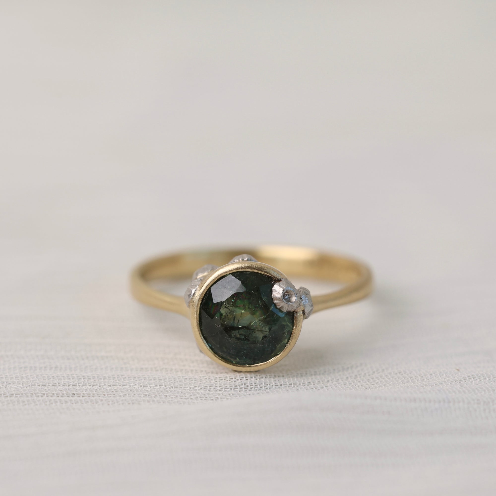 Gold ring with a green gemstone on a light fabric background