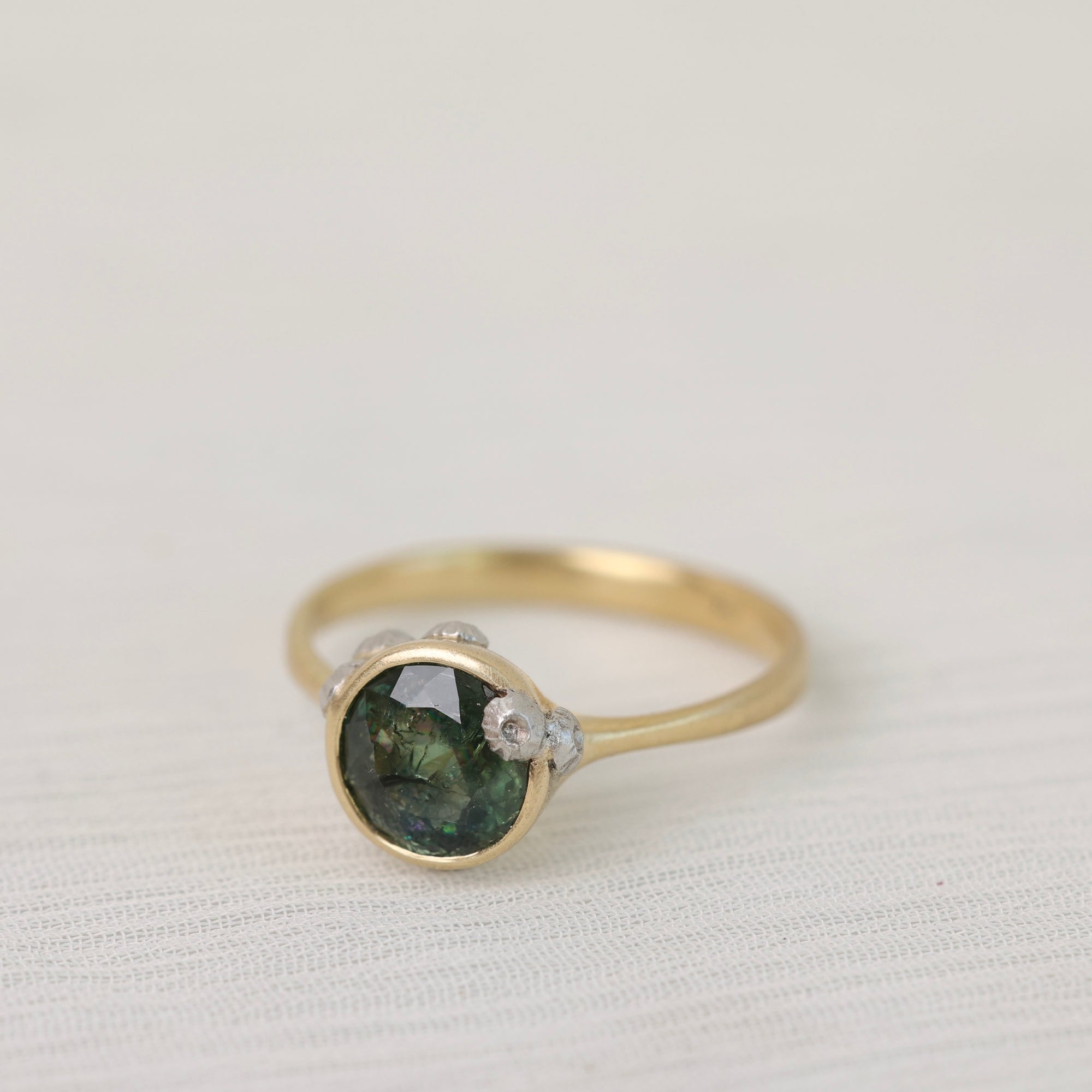 Gold ring with a green gemstone on a light fabric background
