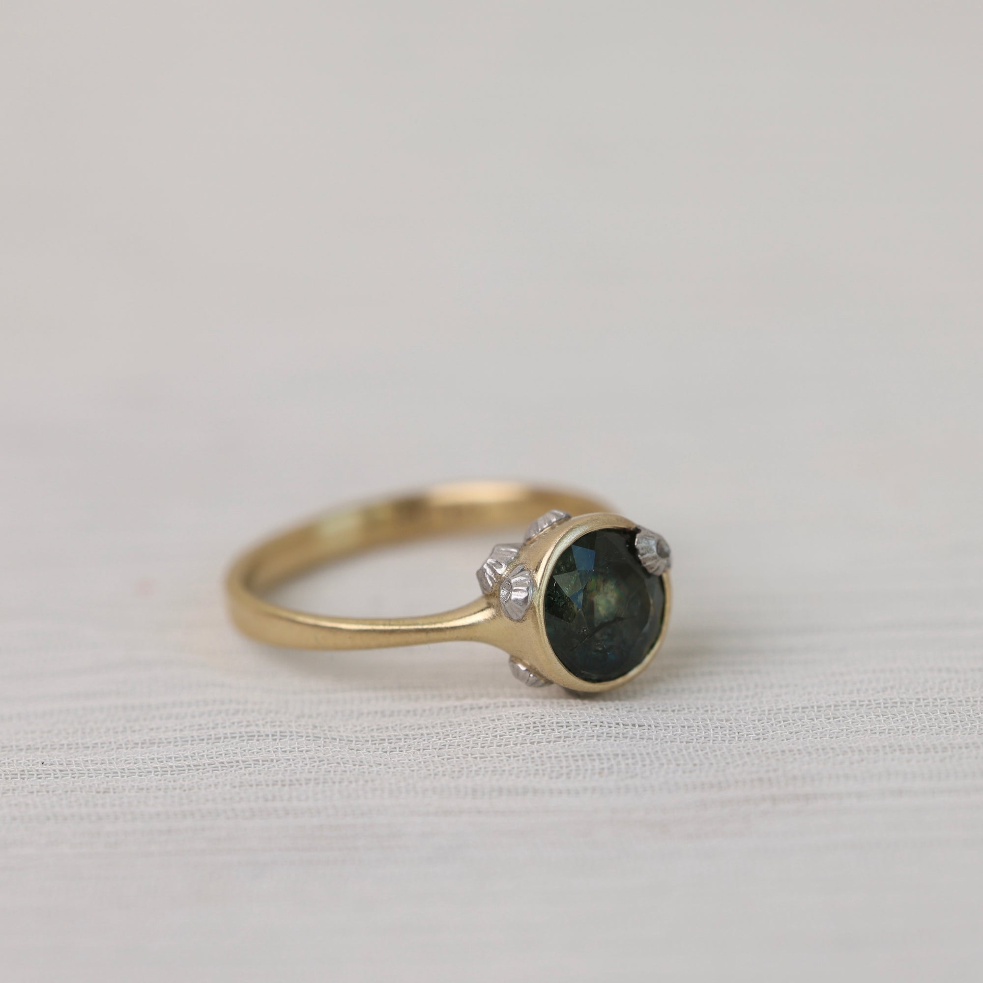 Gold ring with a dark gemstone and small barnacles on a light fabric background