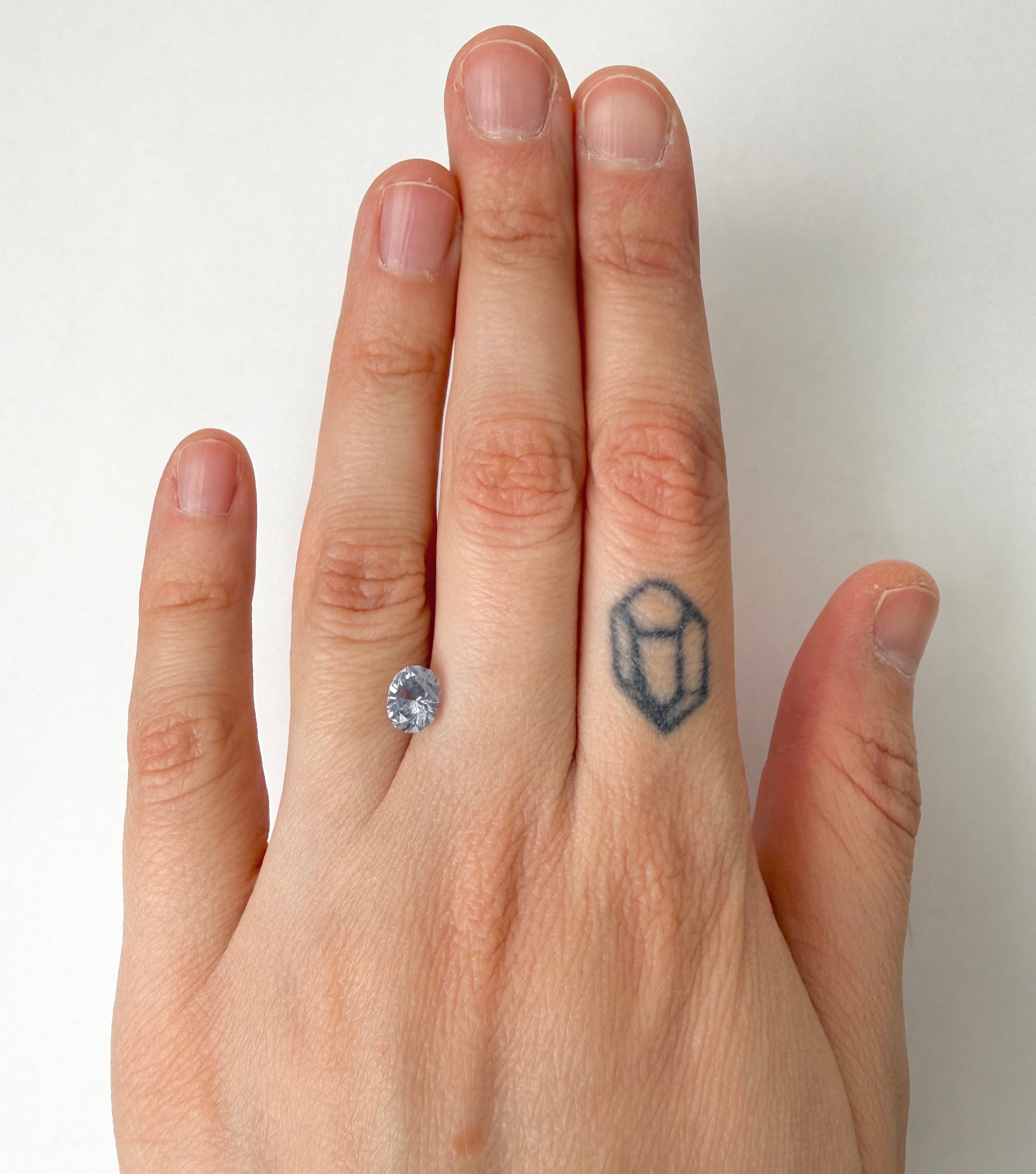 Hand with a stone ring on a finger and a small tattoo on another finger against a white background