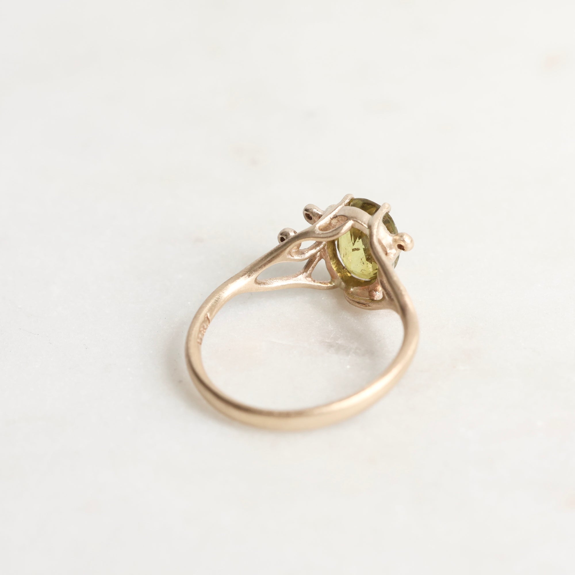 Gold ring with a green gemstone on a light gray background