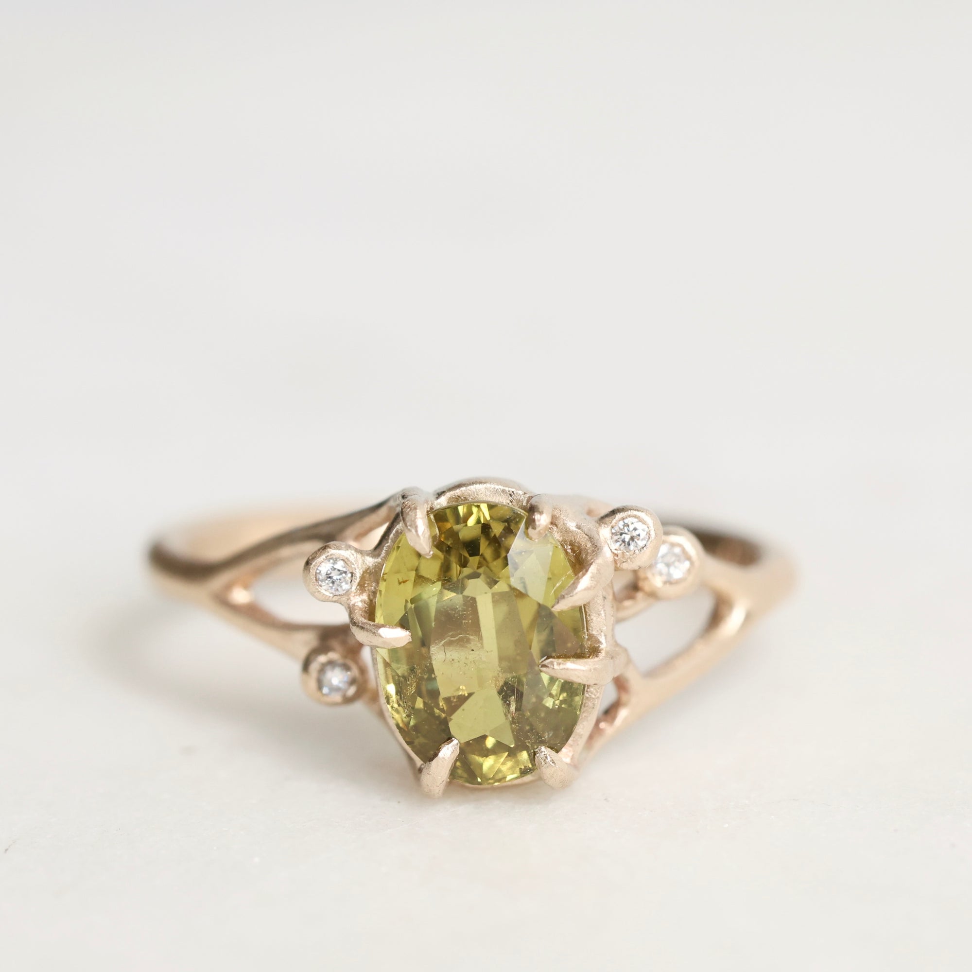 Gold ring with a green gemstone and small diamonds on a light gray background
