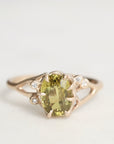 Gold ring with a green gemstone and small diamonds on a light gray background