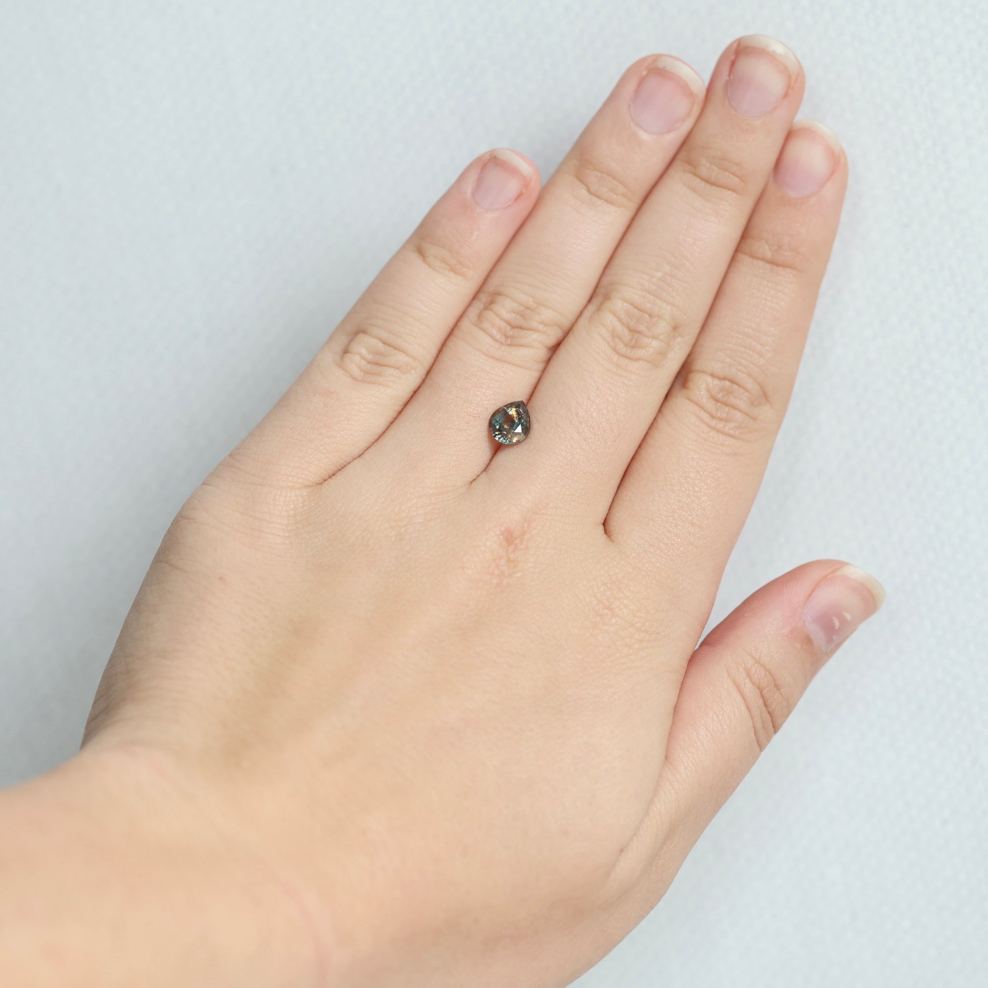 A close-up of a person's hand wearing a small dark gemstone ring on the ring finger, set against a plain light gray background.