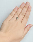 A close-up of a person's hand wearing a small dark gemstone ring on the ring finger, set against a plain light gray background.