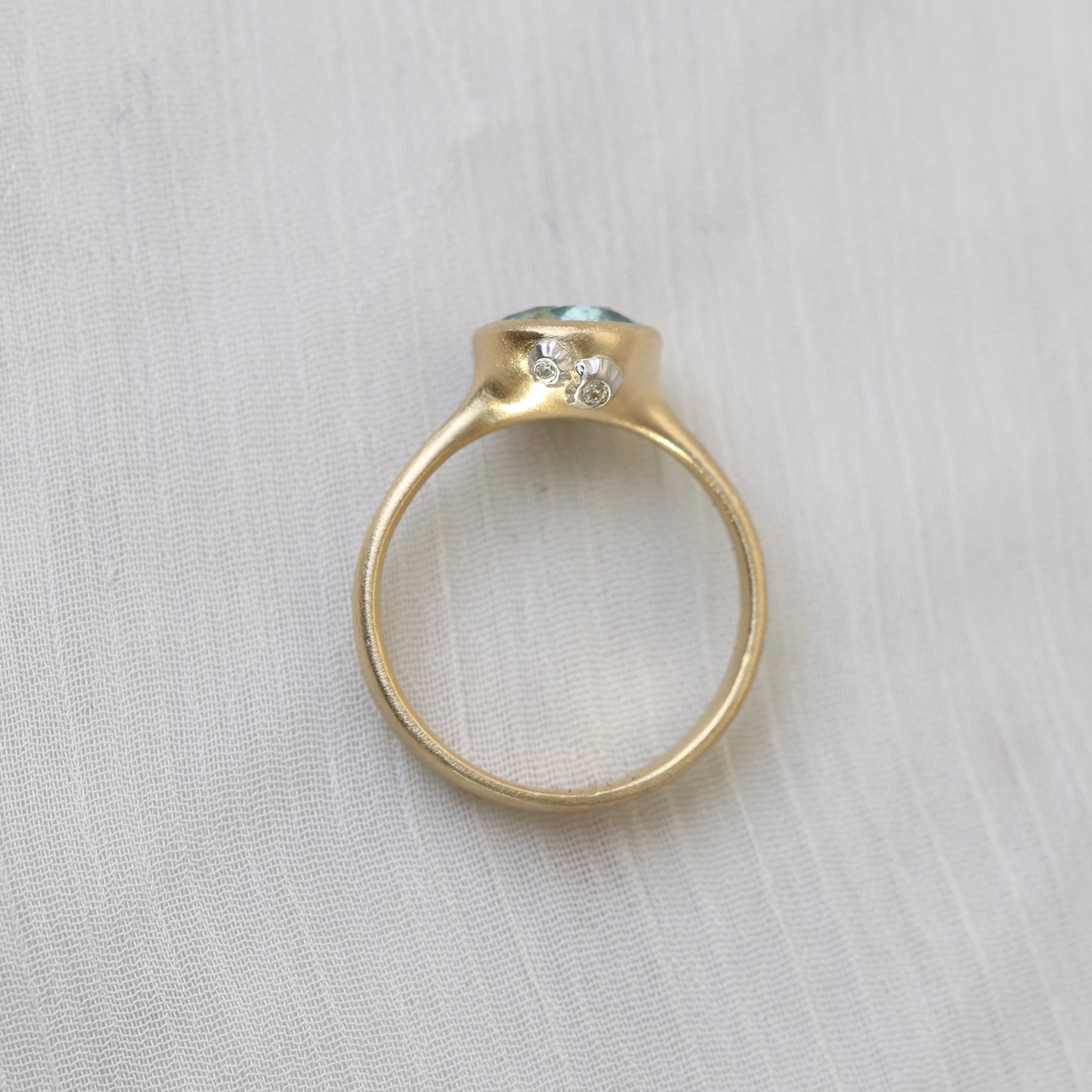 Gold ring with a central gemstone and smaller diamonds on a light fabric background
