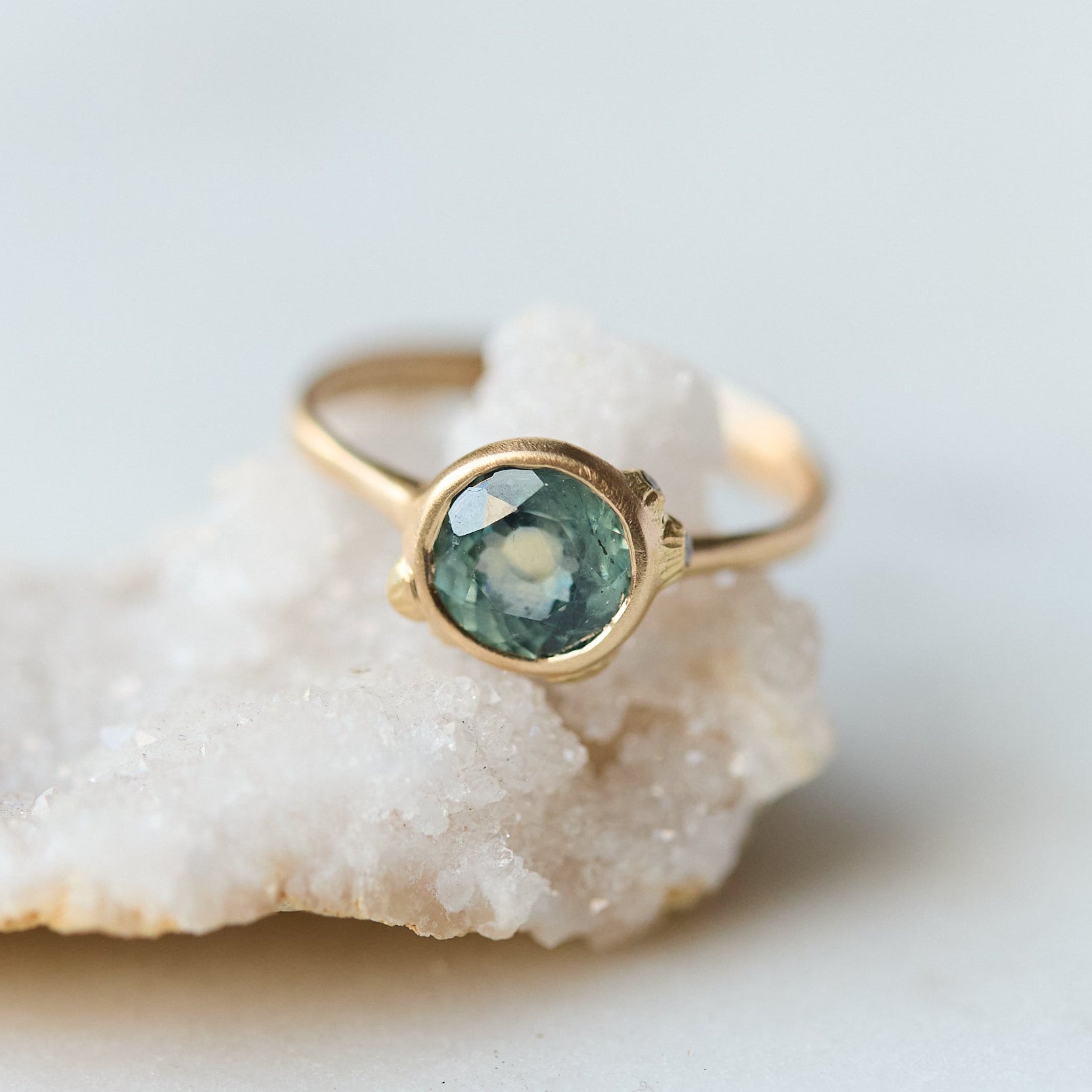 Gold ring with a green gemstone on a white stone surface