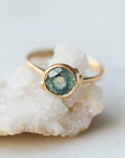 Gold ring with a green gemstone on a white stone surface