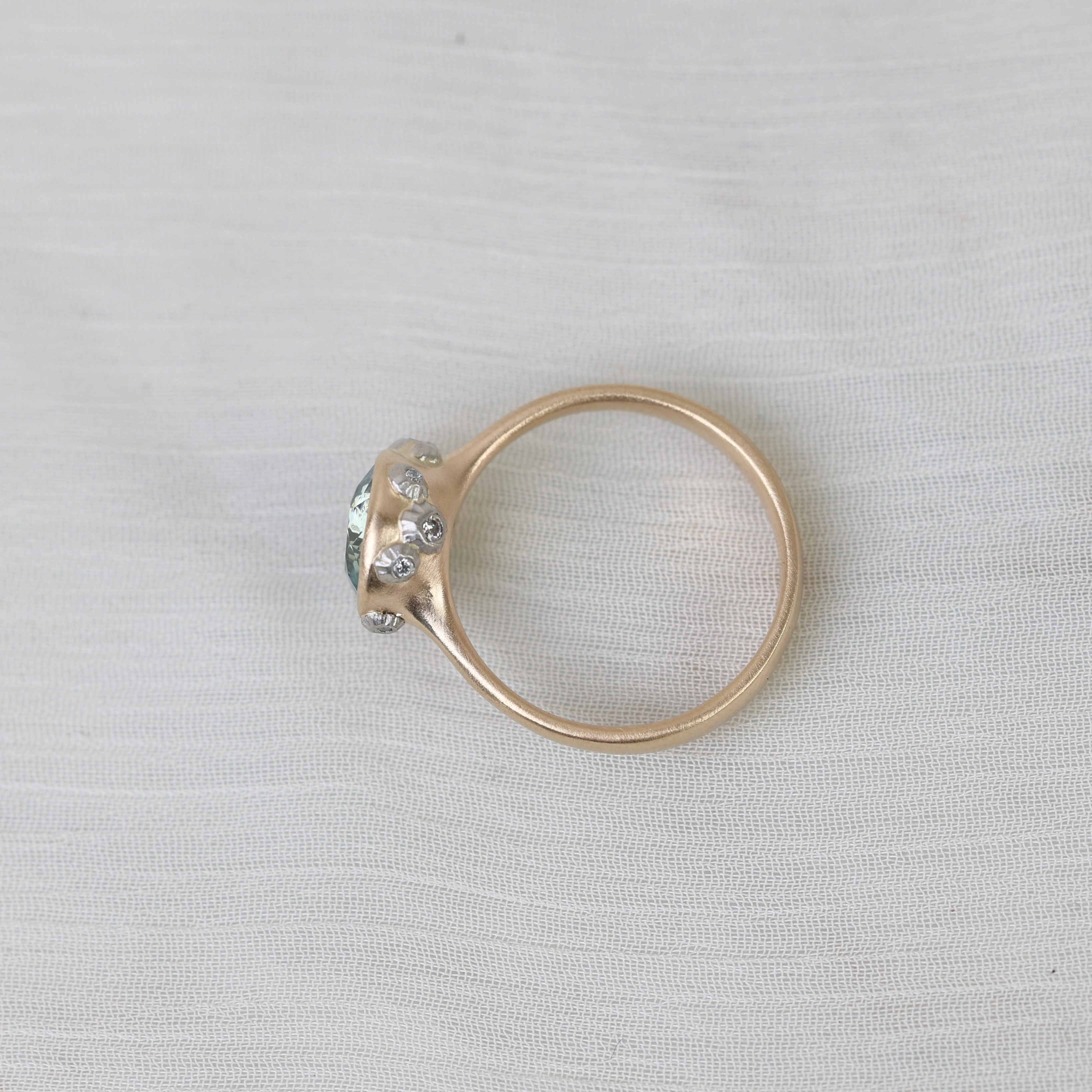 Gold ring with a central gemstone and smaller stones on a light gray background