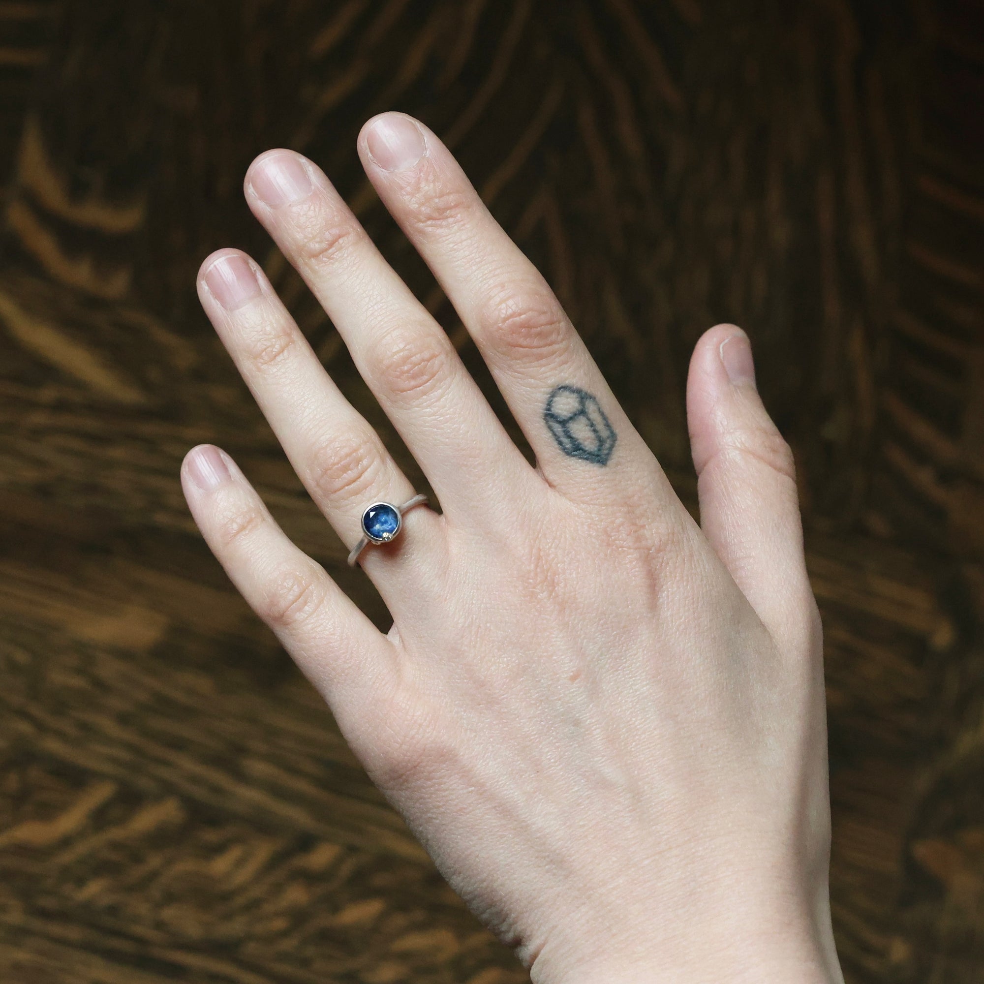 Hand with a blue gemstone ring and matching tattoo on a wooden surface