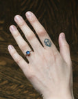 Hand with a blue gemstone ring and matching tattoo on a wooden surface