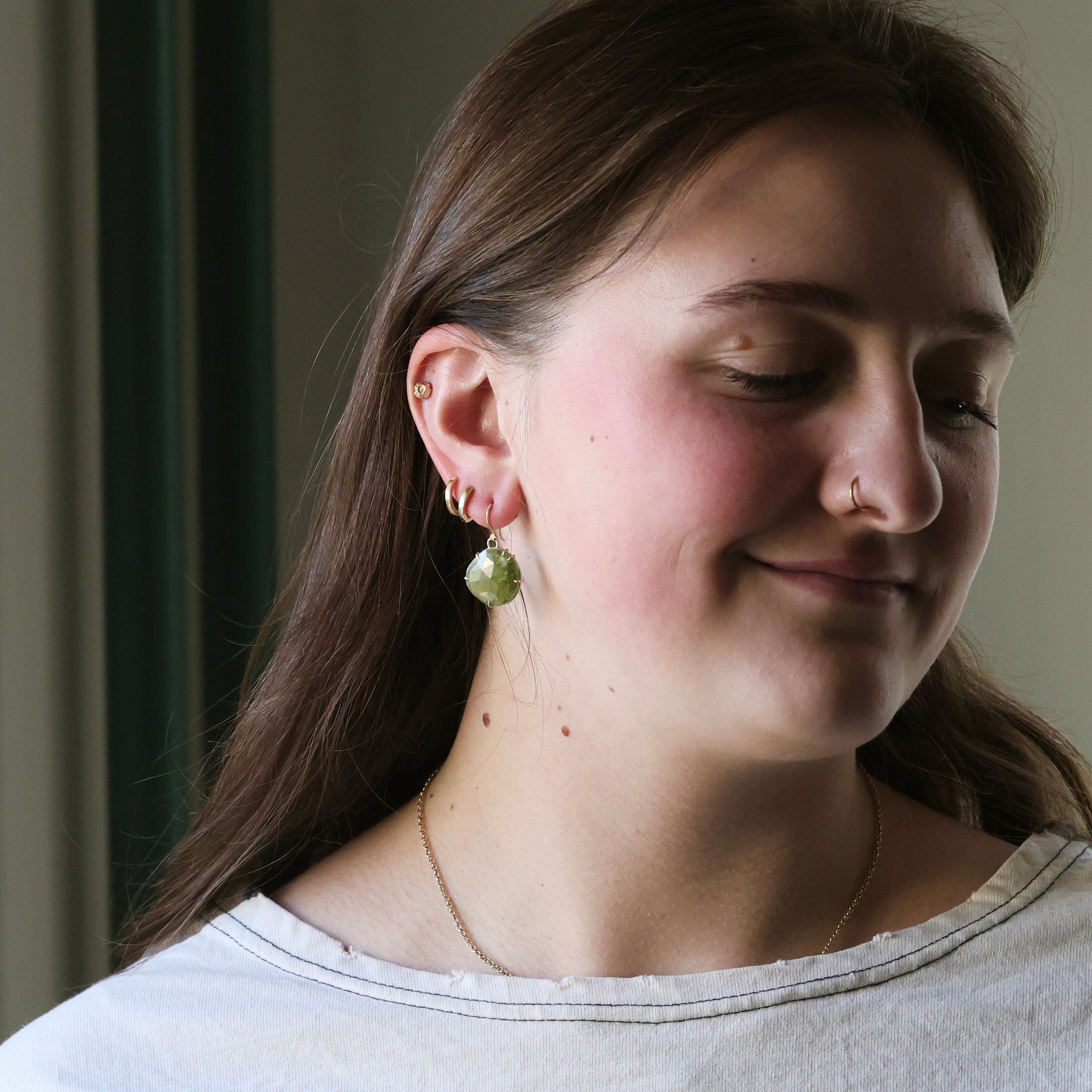 Woman wearing green earrings with a neutral background