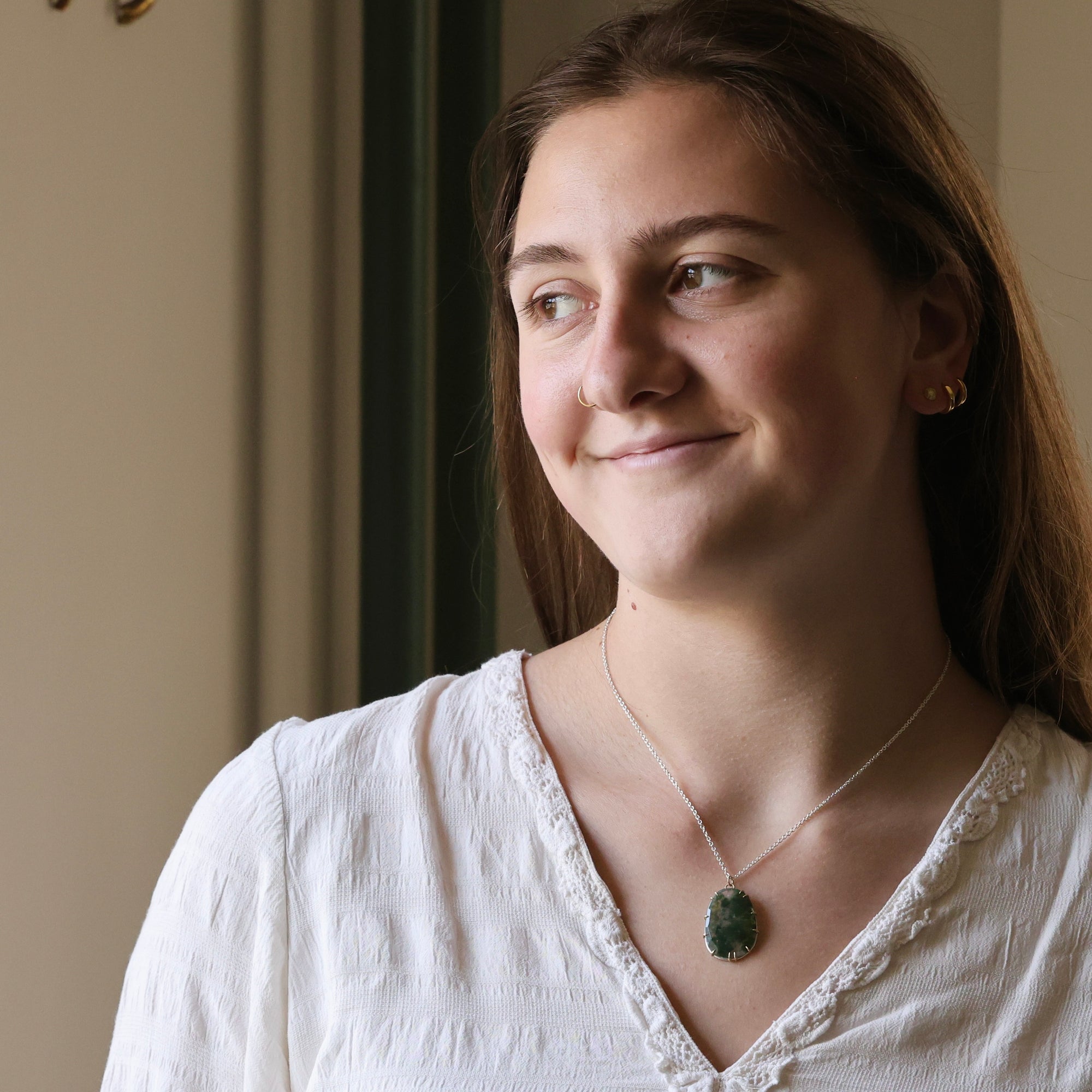 Woman wearing a white blouse with a necklace, standing indoors.
