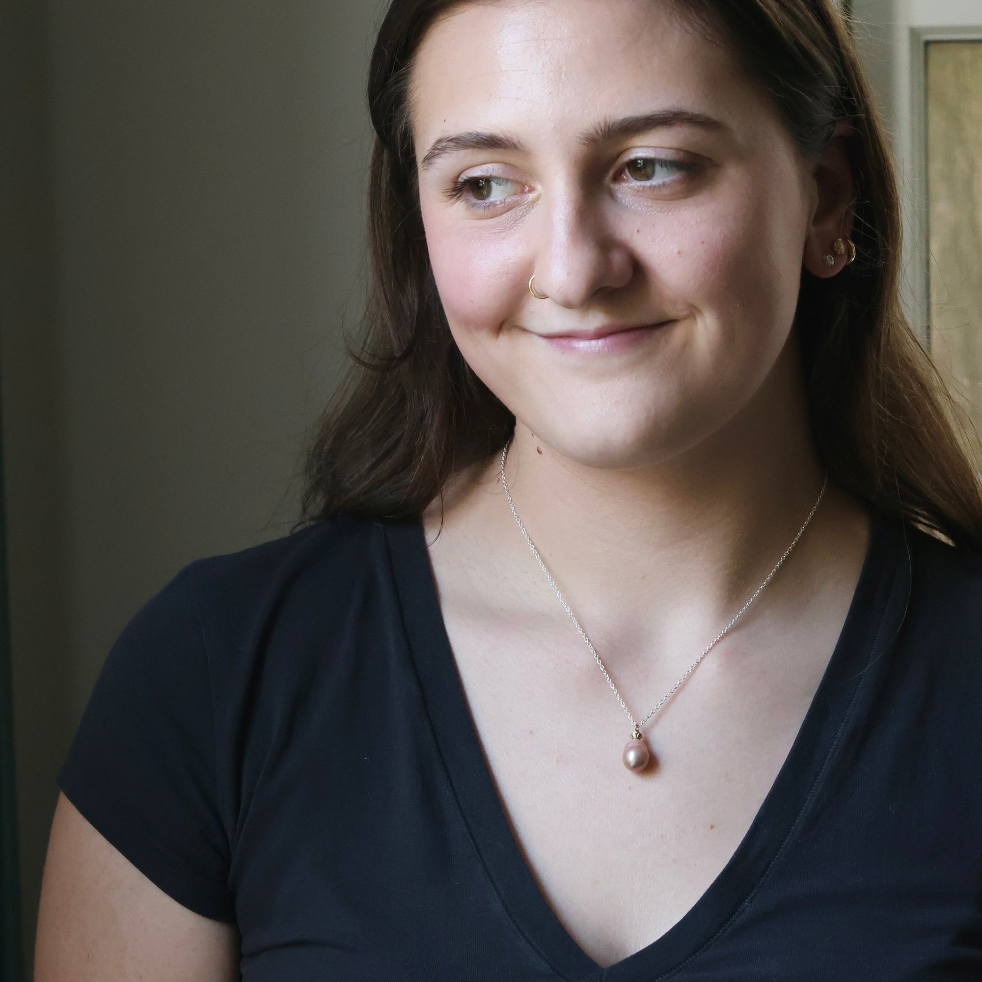 Woman wearing a black top and a necklace with a pendant indoors.