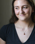 Woman wearing a black top and a necklace with a pendant indoors.
