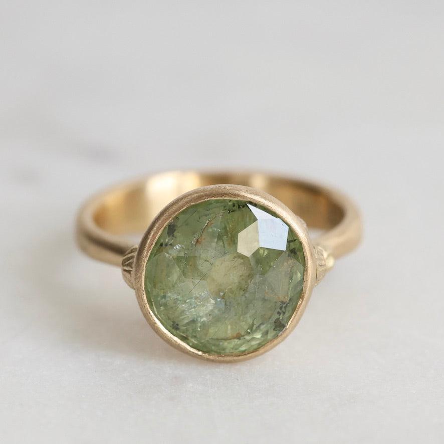 Gold ring with a green gemstone on a light gray background