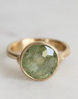 Gold ring with a green gemstone on a light gray background