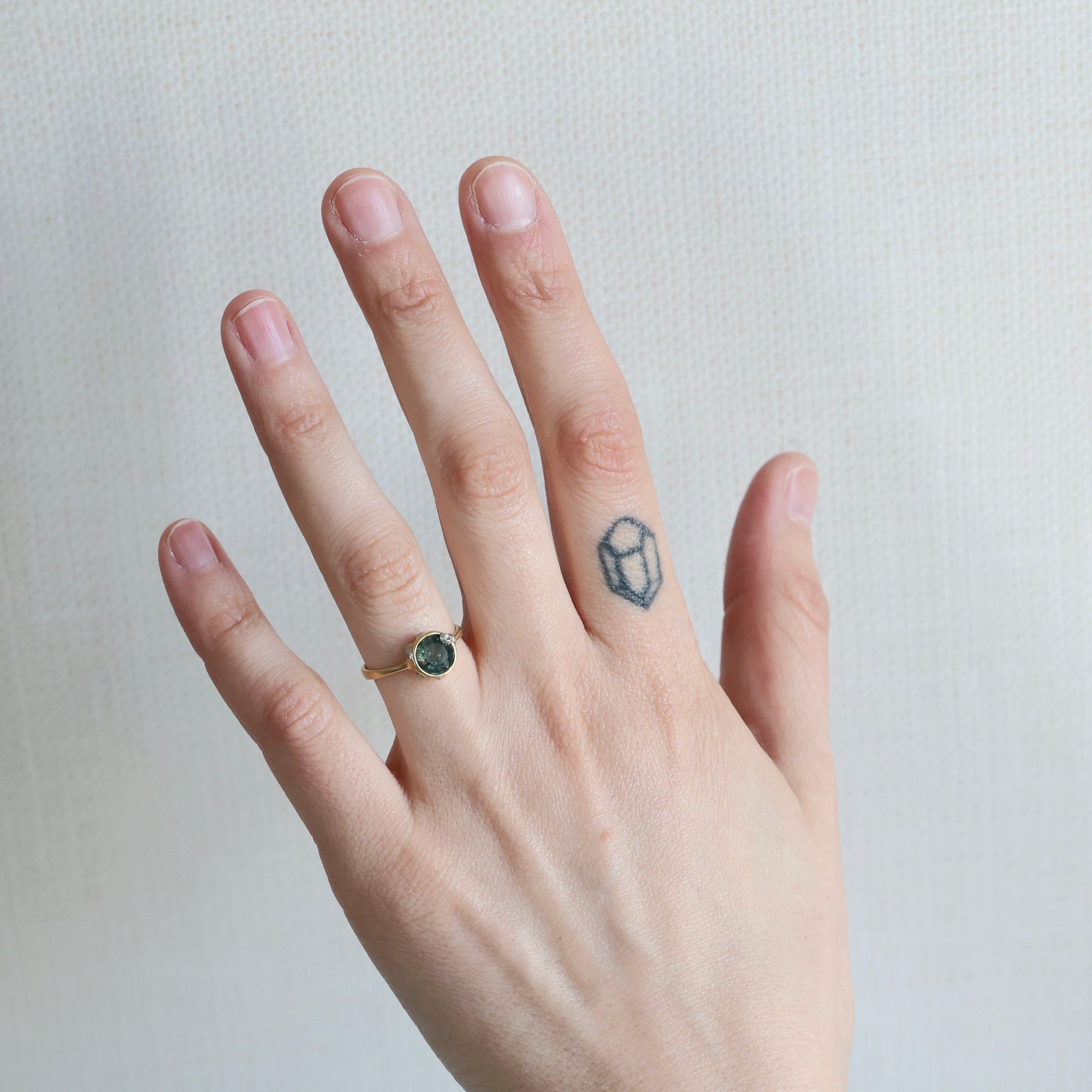 Hand with a ring and a small tattoo on a plain background