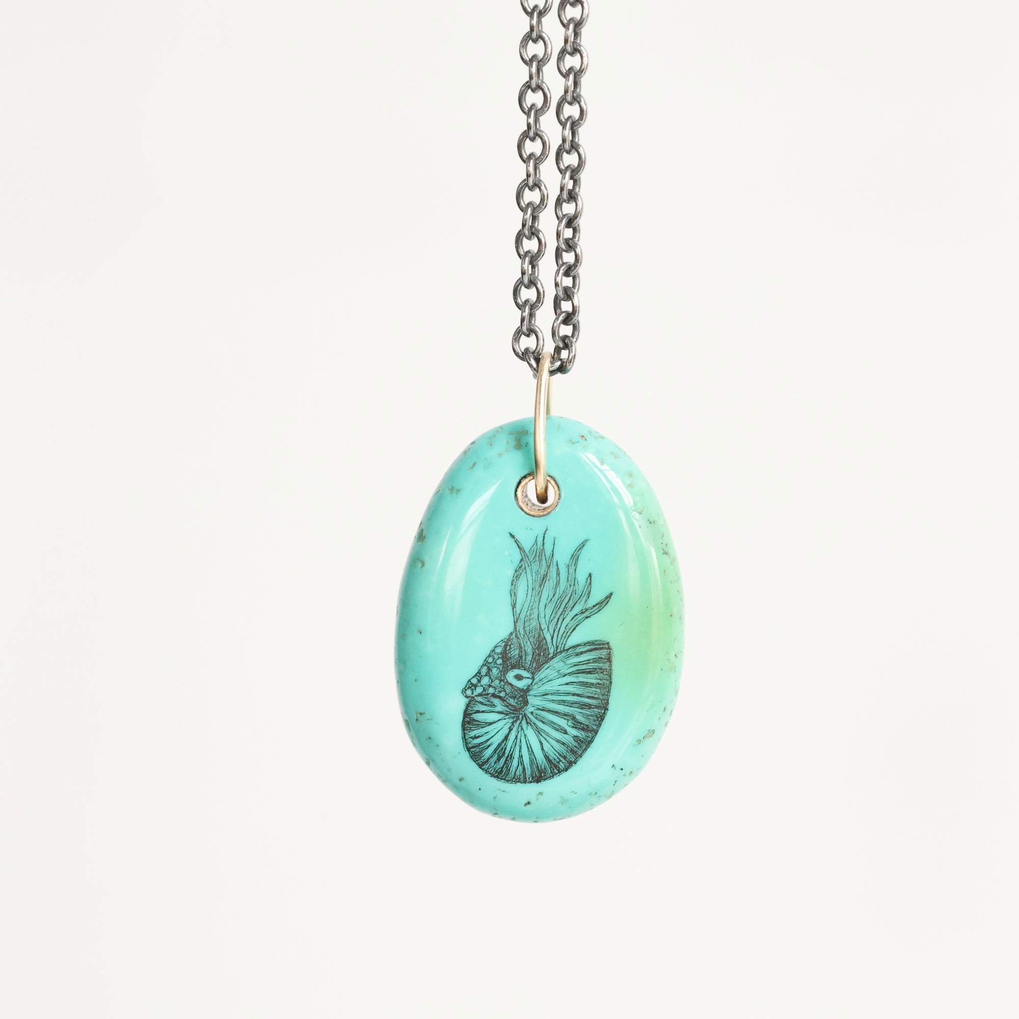 Necklace with a turquoise pendant featuring a black engraved design on a white background