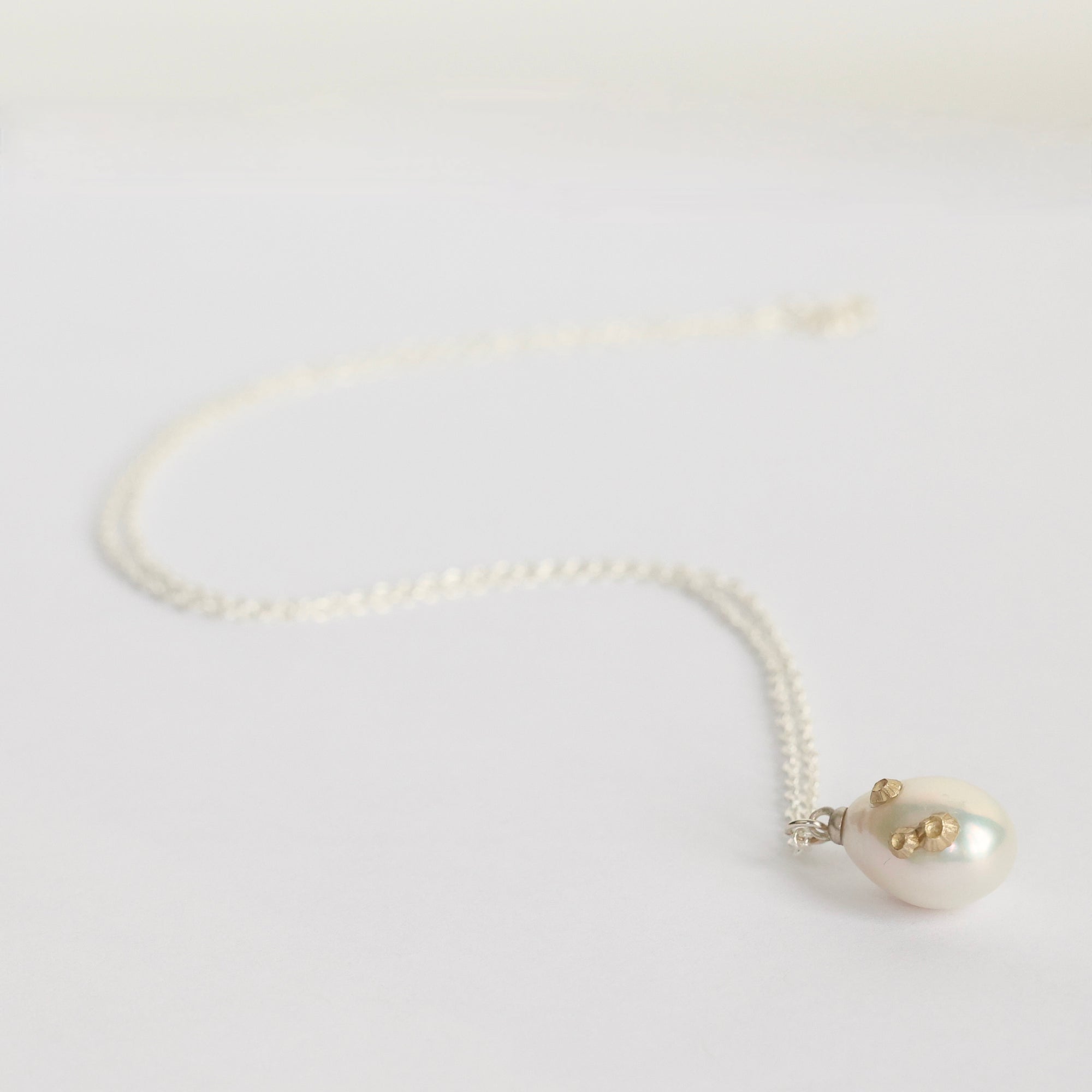 Pearl necklace with a heart-shaped pendant on a light gray background