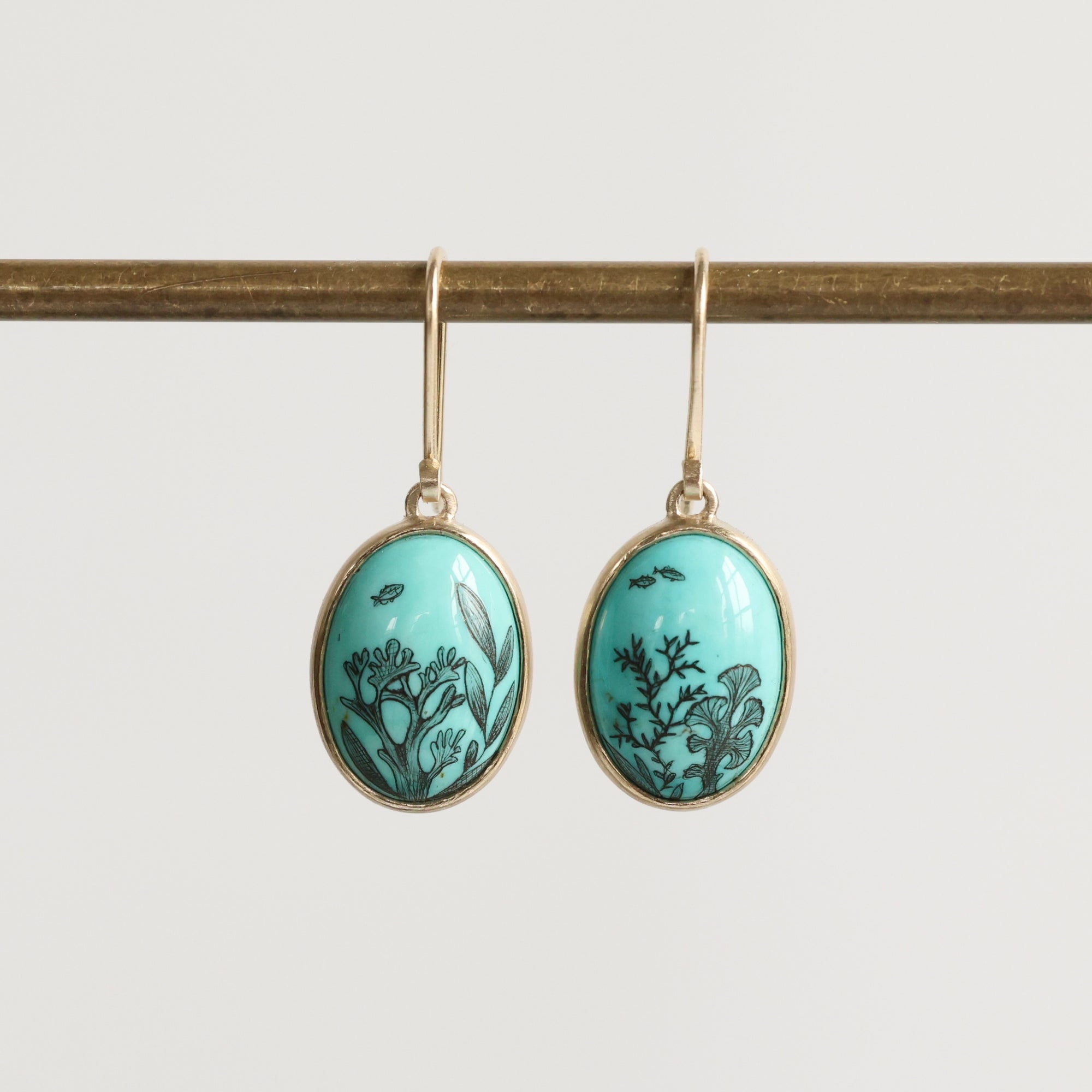 Pair of earrings with turquoise oval stones featuring black floral designs on a white background.